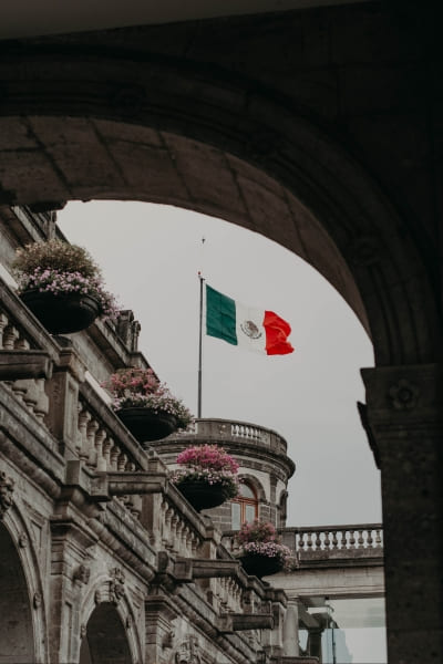 Edifício clássico em que aparece uma bandeira mexicana hasteada. A Santy ajuda você com seu visto mexcano.